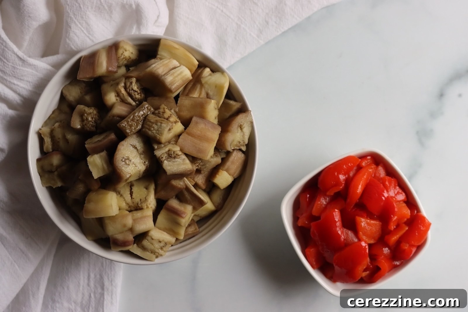 Chopped roasted eggplant and red peppers in two bowls for caponata
