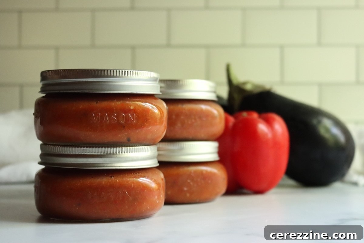 Sealed jars of canned ajvar stacked two high beside a red bell pepper and an eggplant