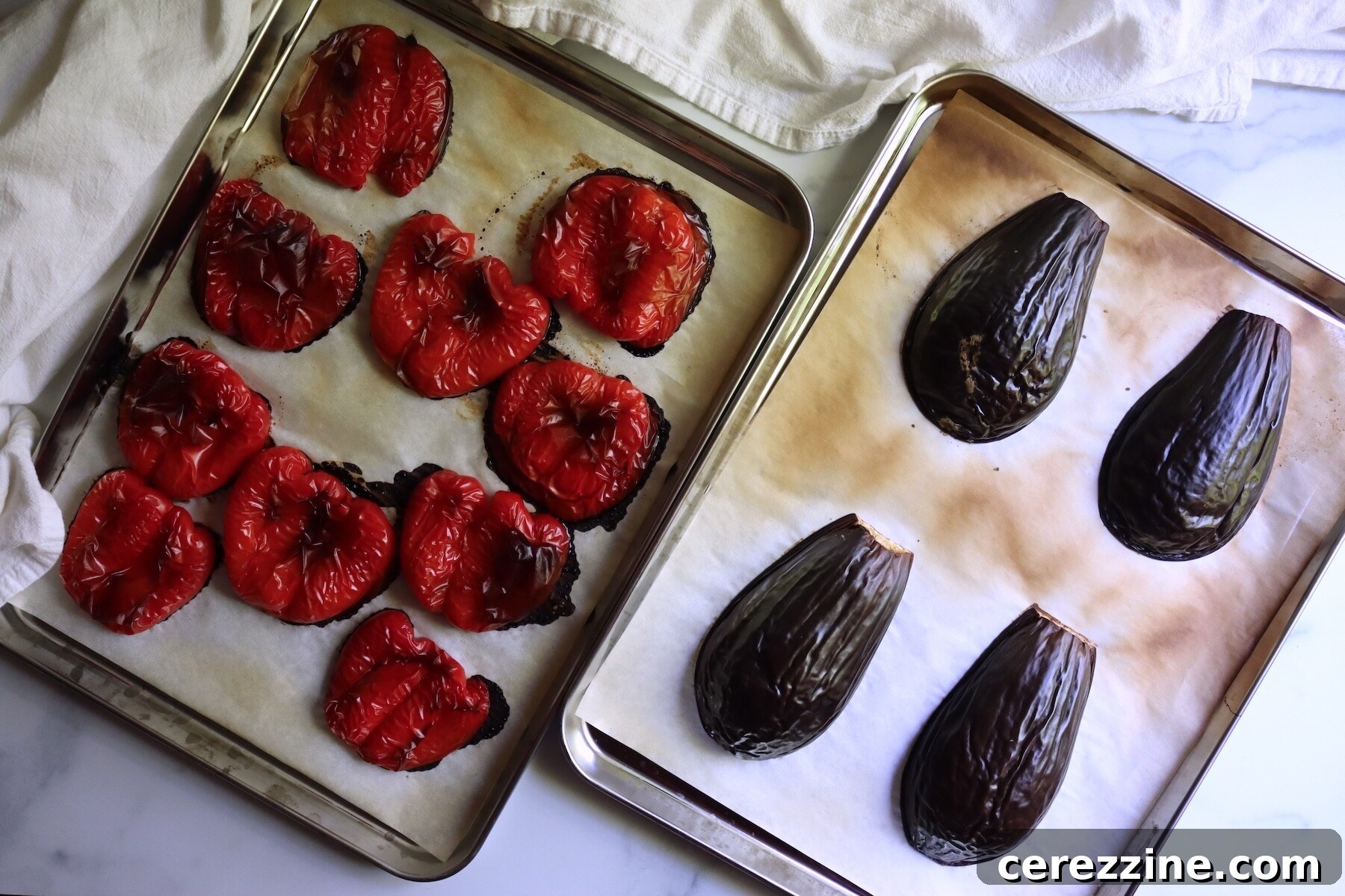 Red bell pepper halves and eggplant halves roasted skin side up on two parchment-lined baking sheets