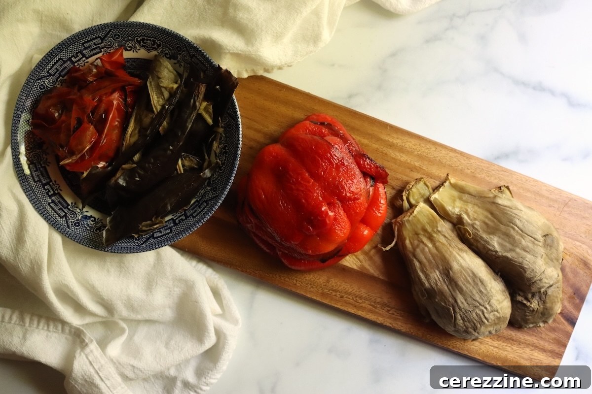 Peeled roasted red peppers and scooped eggplant on a cutting board, with the skins in a bowl