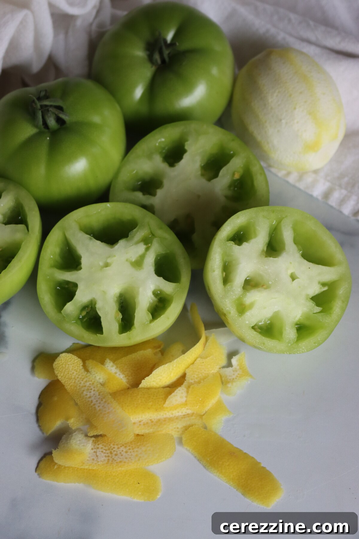 Green tomatoes cut in half to check the seeds, next to strips of lemon peel