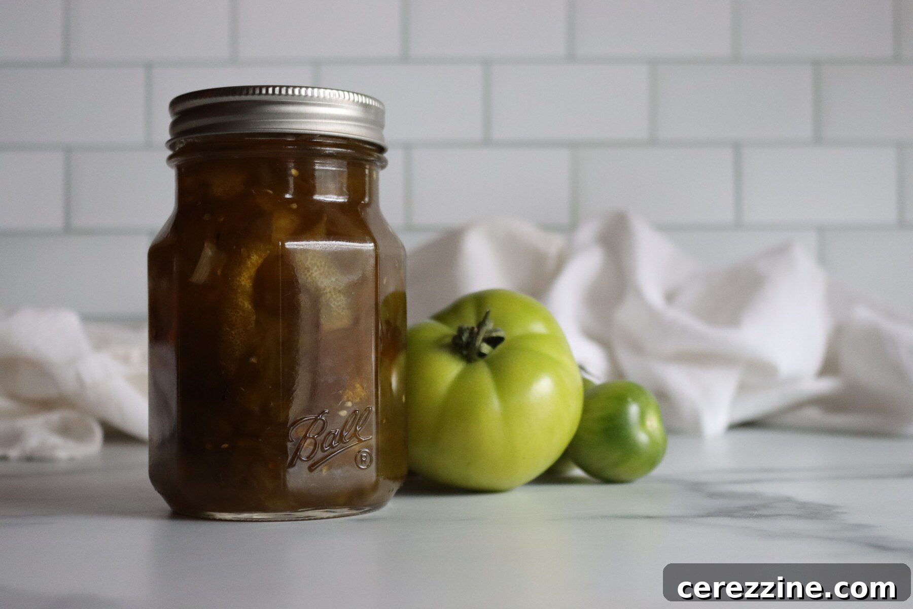 Pint jar of Italian green tomato preserves on a marble counter with green tomatoes