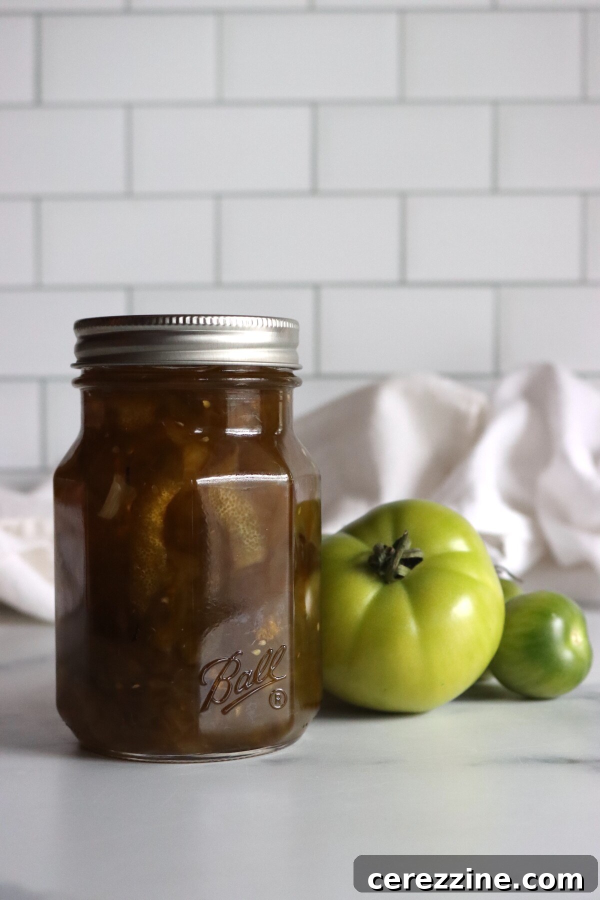 Pint jar of green tomato preserves next to unripe green tomatoes