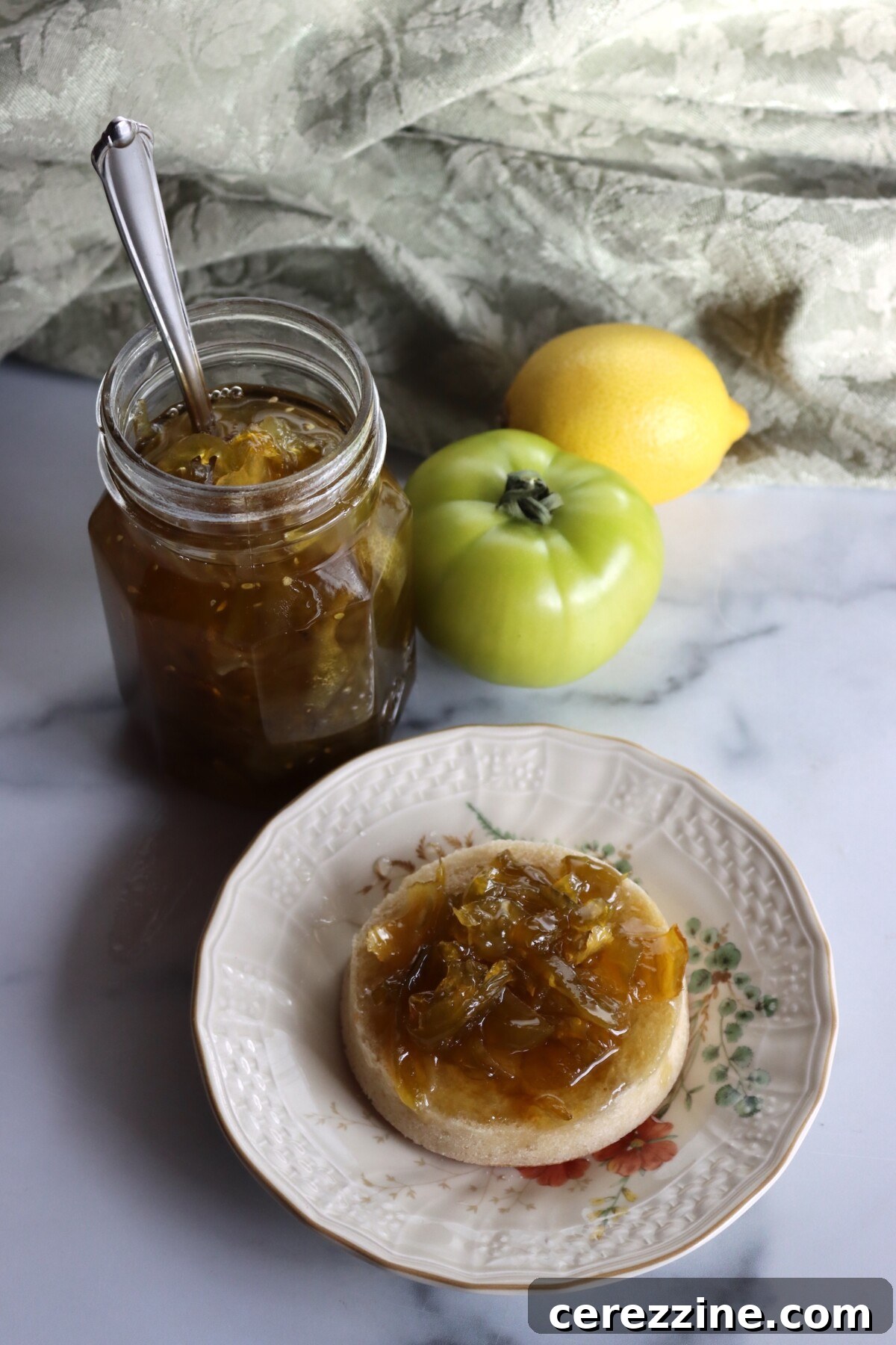 Open jar of Italian green tomato preserves with a spoon, and preserves spread on an English muffin
