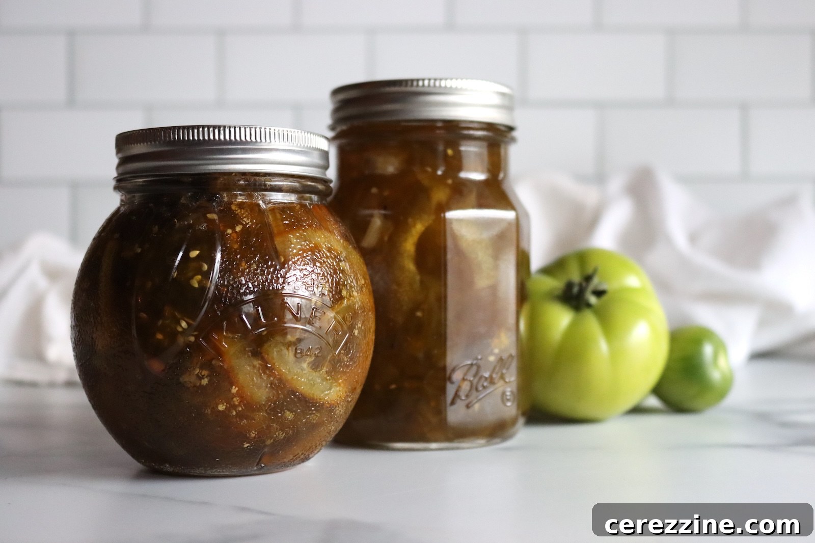 Round jar of green tomato marmalade in front of a pint jar of green tomato preserves
