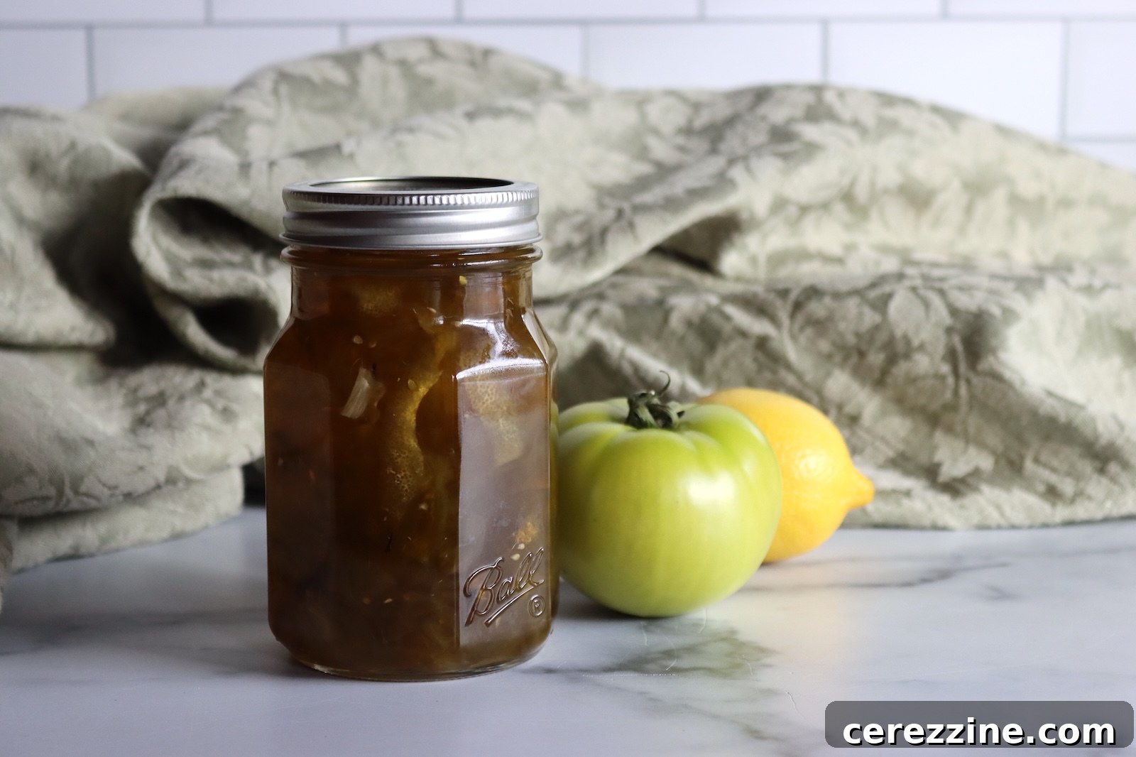 Pint jar of green tomato preserves with a green tomato and a lemon